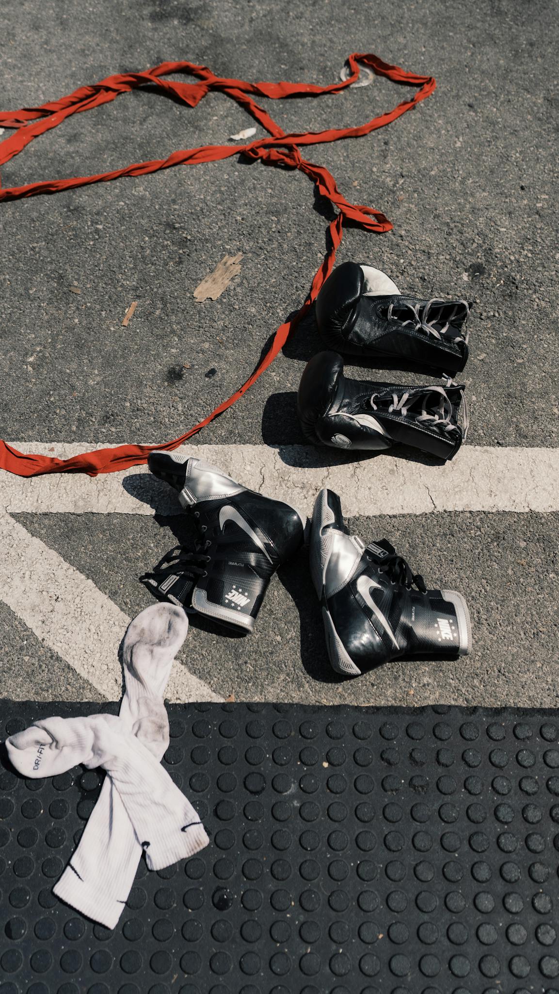 Boxing gloves and shoes with hand wraps on urban asphalt surface.