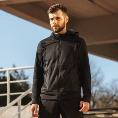 Portrait of a confident young sportsman in earphones standing outdoors
