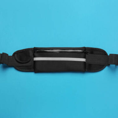 Stylish black waist bag on light blue background, top view