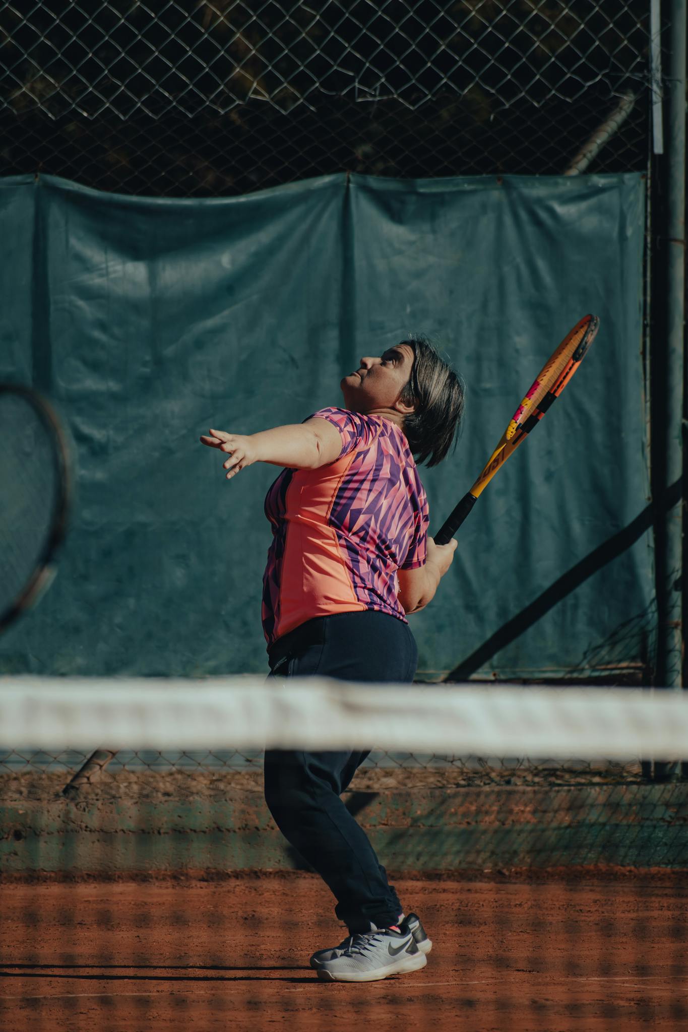 Woman in activewear preparing to serve on a tennis court in daylight.